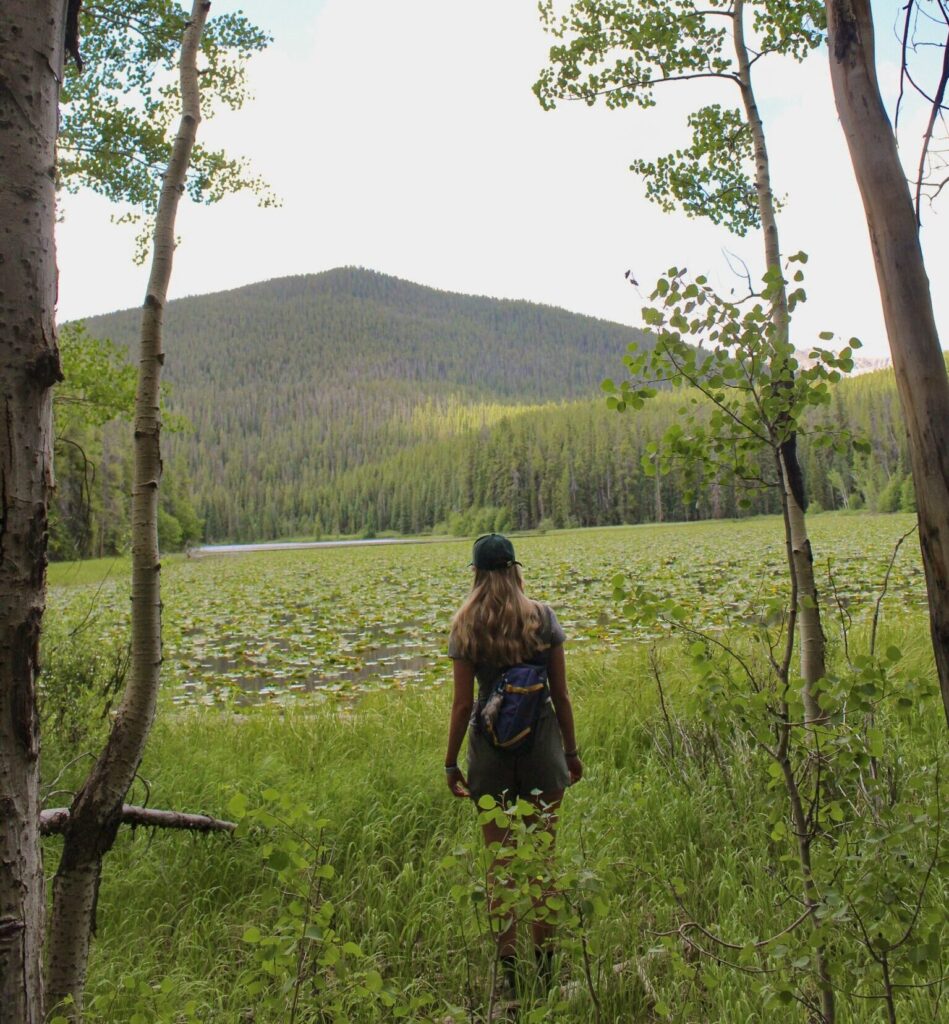 Ashley standing in a clearing, looking onto a lake and distant mountain.