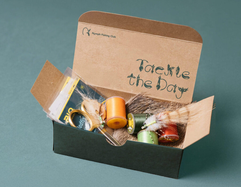Box of fly fishing equipment. It reads: "tackle the day".