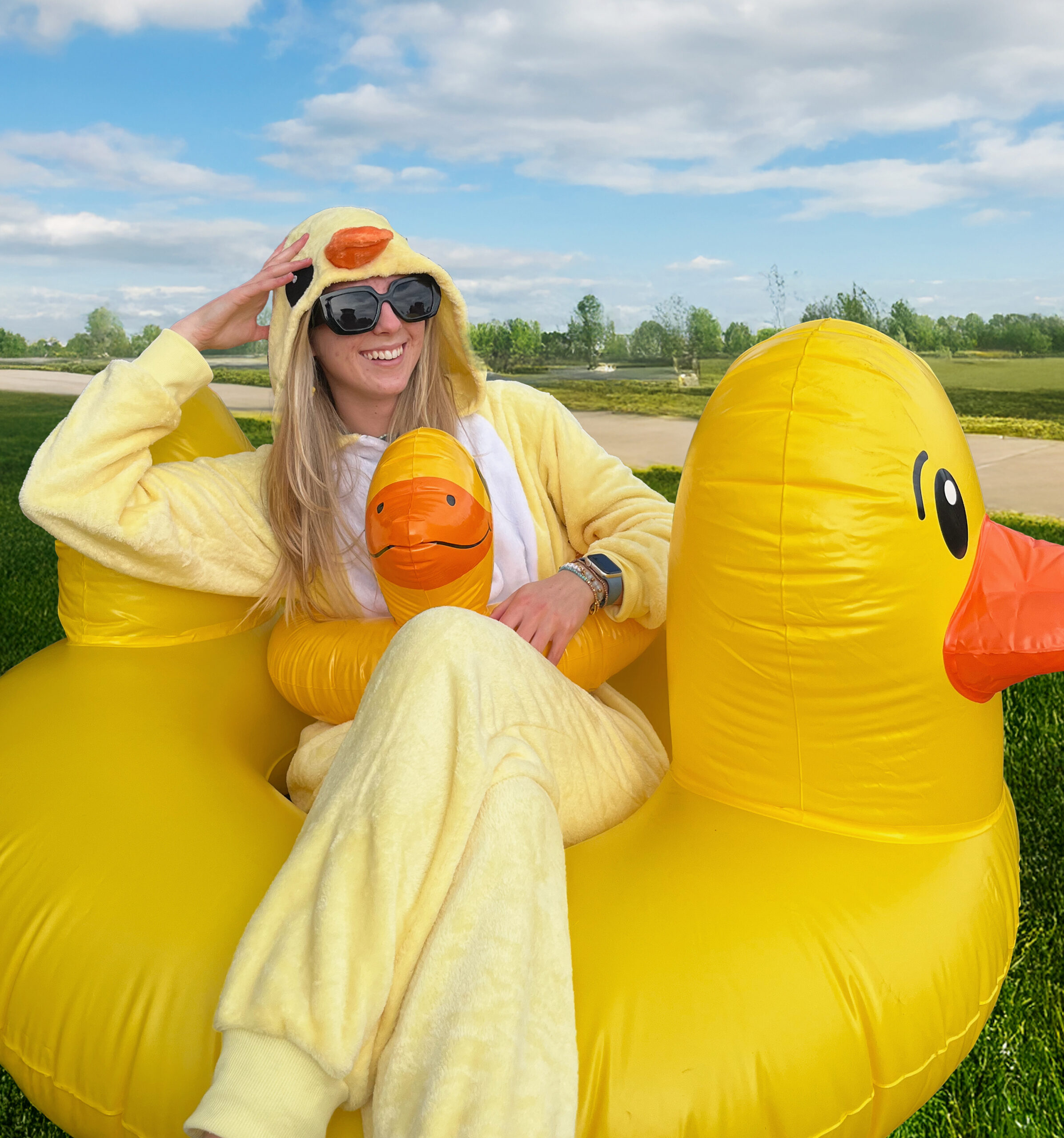 After edits. Girl wearing duck onesie sitting inside duck floatie in a grass field.
