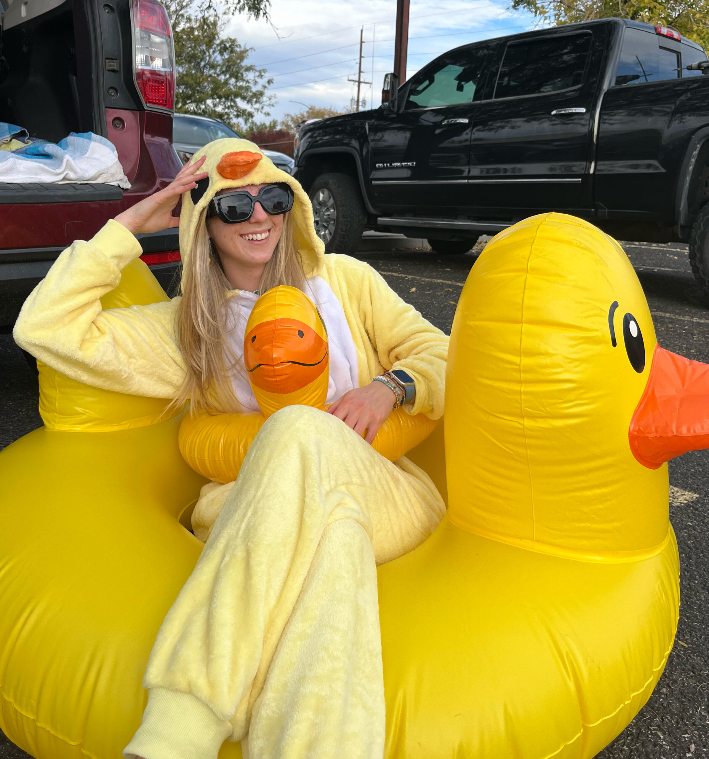 Before edits. Girl wearing duck onesie sitting inside duck floatie in a parking lot.
