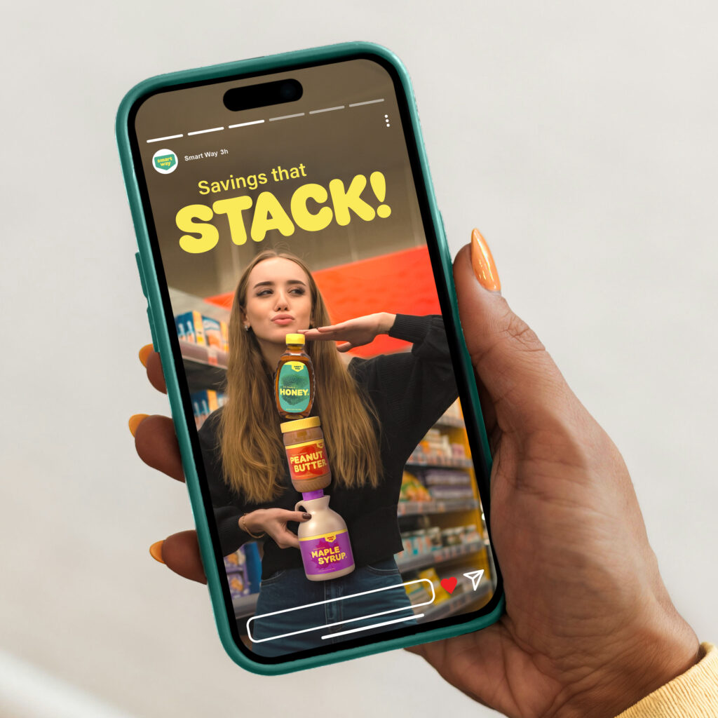 Hand holding a smartphone displaying a colorful Smart Way peanut butter, honey, and syrup advertisement against a grocery isle background.