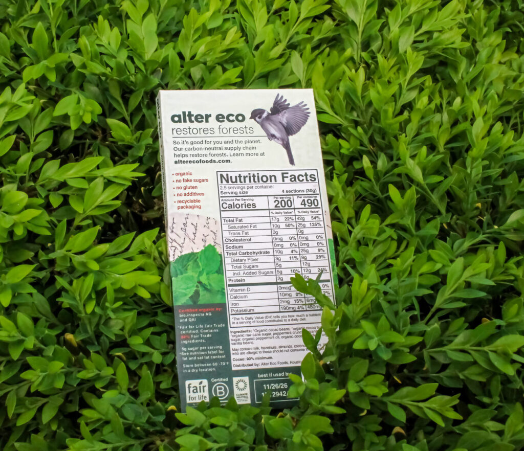 Alter Eco chocolate packaging standing upright in grass surrounded by bright green foliage.